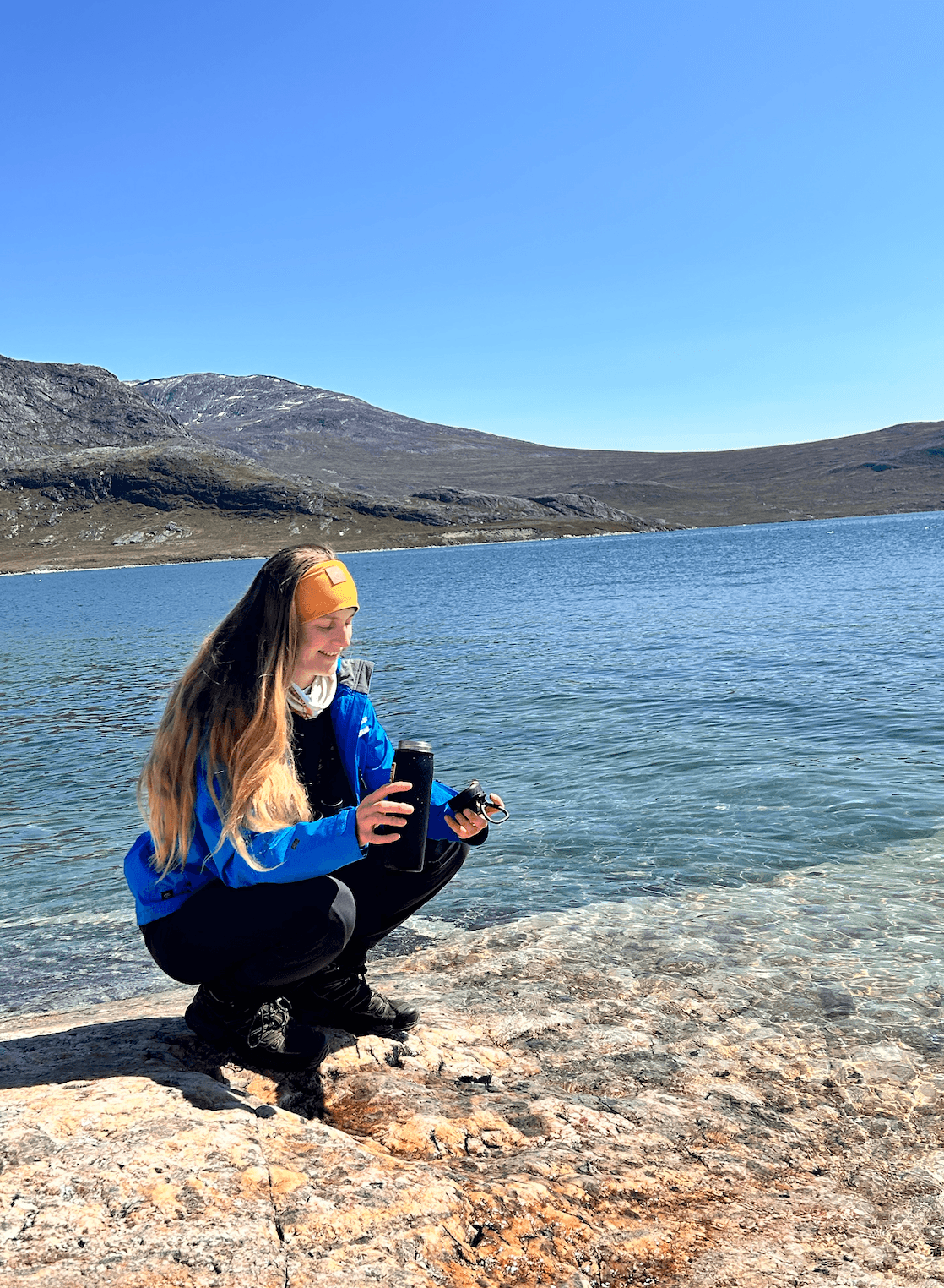 Jesse Wallace collecting a water sample beside a Greenlandic fjord
