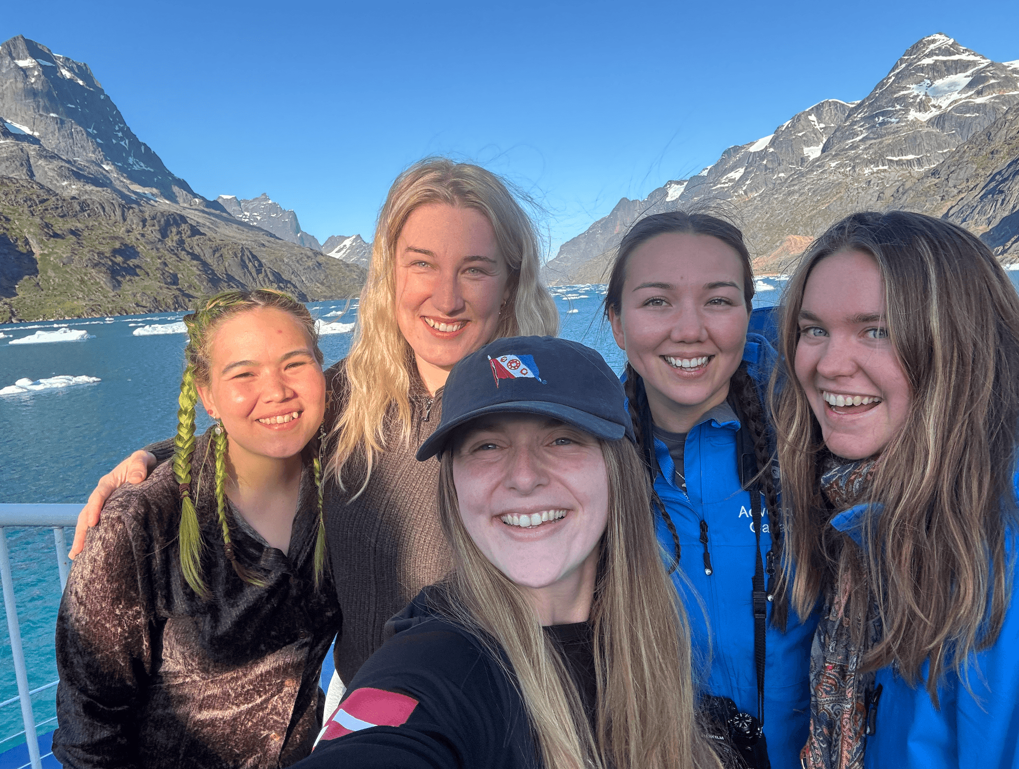 Young Explorers on board with Greenlandic mountains and icebergs behind them
